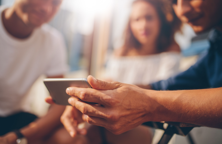 Photo of young group of coworkers looking at data on a mobile phone to illustrate the concept of driving business using digital in 2023.