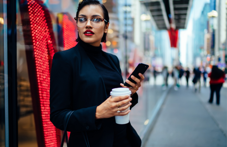 Woman with mobile phone and coffee leaning against wall to illustrate the State of Digital Q3 2023